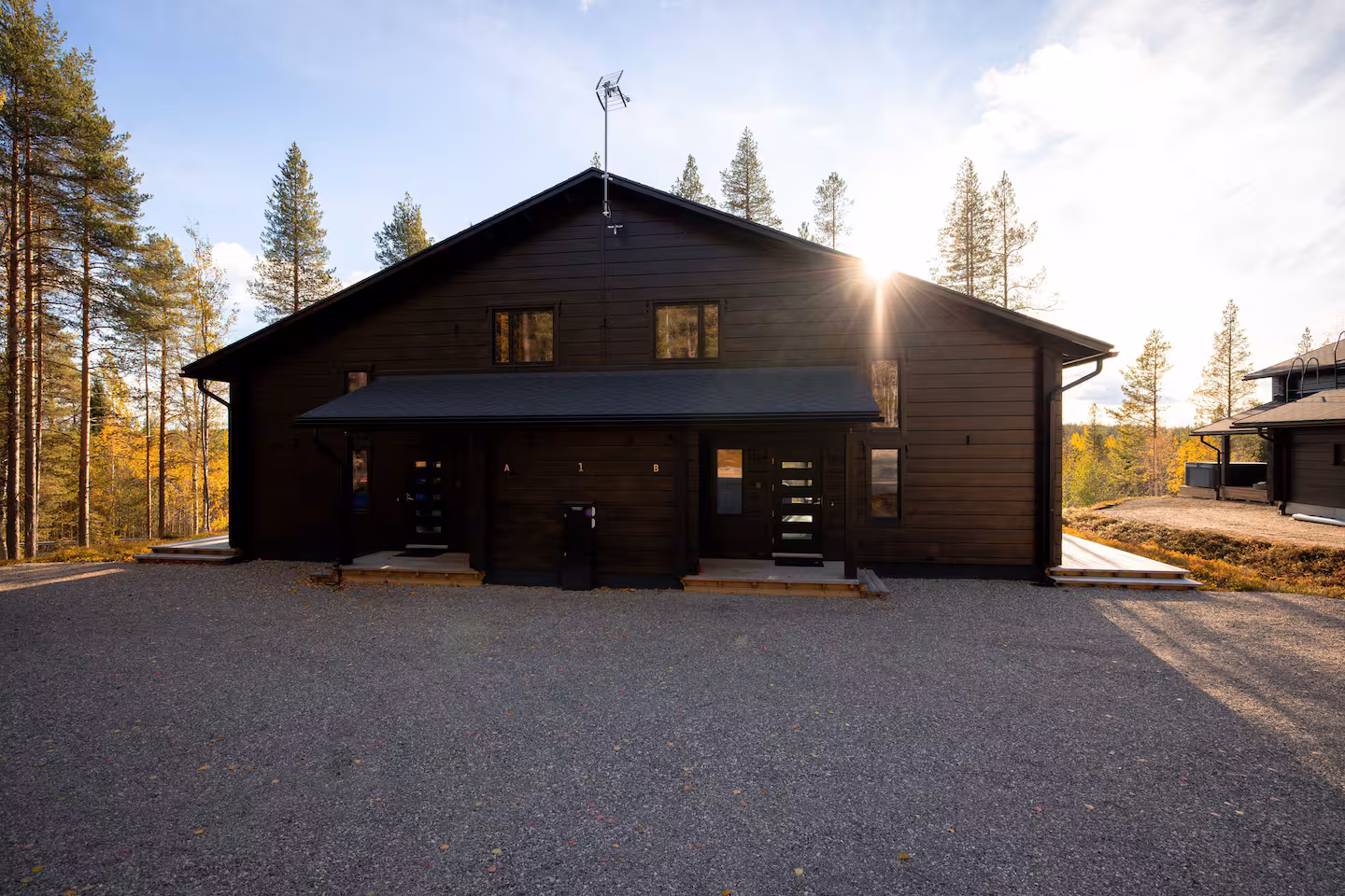Dark timber villa with a gravel forecourt, backlit by low autumn sun